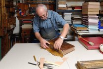 Hombre mayor reparando espina dorsal de libro antiguo en taller de encuadernación tradicional - foto de stock