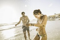 Couple adulte moyen portant un bikini et un short éclaboussant sur la plage, Cape Town, Afrique du Sud — Photo de stock