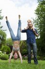 Mother doing handstand in garden next to family — Stock Photo