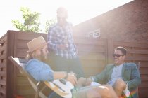 Três amigos do sexo masculino conversando e tocando guitarra na festa no telhado — Fotografia de Stock