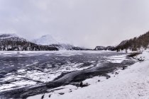 Lago congelado y montañas cubiertas de nieve bajo el cielo nublado - foto de stock