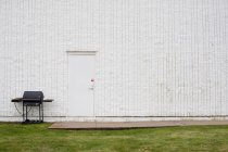 Барбекю на зеленій траві біля білої будівельної стіни — стокове фото