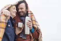 Casal ao ar livre sob cobertor beber bebida quente de garrafa térmica — Fotografia de Stock
