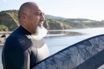Зрелый мужчина-серфер с доской для серфинга, наблюдающий за морем — стоковое фото