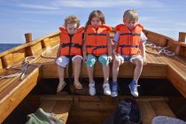 Tre bambini in giubbotto salvagente seduti in barca — Foto stock