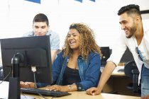 Drei befreundete Studenten lachen und schauen auf den PC im Klassenzimmer — Stockfoto