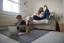 Братья играют на ковре в гостиной, родители на диване — стоковое фото