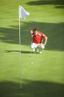 Vista frontal del golfista agachándose frente a la bandera de golf considerando la estrategia - foto de stock