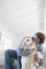 Молодой человек в гостиной обнимает золотистую собаку-ретривера — стоковое фото