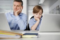 Father and son using laptops looking bored — Stock Photo