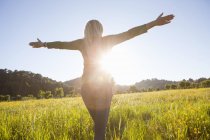 Visão traseira da mulher madura com os braços abertos no prado ao pôr do sol — Fotografia de Stock