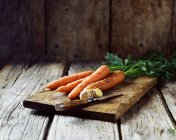 Zanahorias y jengibre sobre tabla de madera con cuchillo - foto de stock