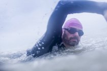 Зрелый человек, плавающий в море в гидрокостюме и очках — стоковое фото