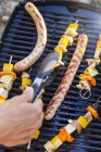 Pessoa que usa pinças para transformar salsichas e kebabs em grelha de churrasco — Fotografia de Stock