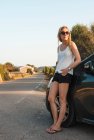 Mujer adulta media apoyada en coche en carretera, Menorca, Islas Baleares, España - foto de stock