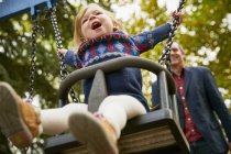 Padre spingendo figlia su altalena parco giochi — Foto stock