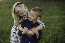 Schwester umarmt Bruder lächelt draußen — Stockfoto