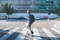 Young man crossing pedestrian crossing with skateboard — Stock Photo