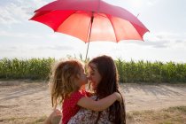 Mother and daughter hugging under red umbrella — Stock Photo
