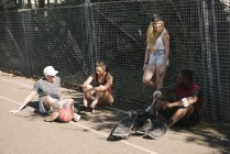 Quatre amis adultes skateboarder assis bavarder sur le terrain de basket-ball — Photo de stock