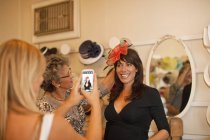 Women taking picture in fancy hat in traditional milliner shop — Stock Photo
