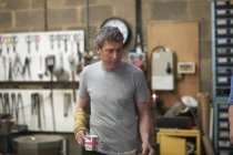 Мужчина, кавказский стеклодув в мастерской, держит кружку — стоковое фото