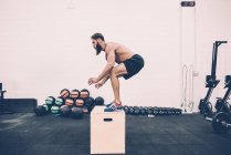 Young male cross trainer jumping on box in gym — Stock Photo