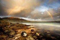 Rainbow stretching over still rural lake — Stock Photo