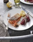Trout steak with radicchio salad leaves, lemon and fork on plate — Stock Photo