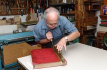 Uomo anziano restauro libro nel tradizionale laboratorio di rilegatura — Foto stock