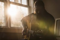 Чоловік грає на гітарі біля вікна — стокове фото
