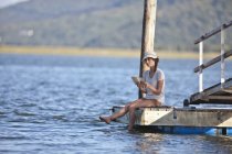 Young woman sitting on jetty, reading book — Stock Photo