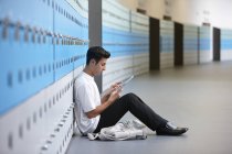 Portrait of teenage schoolboy sitting on floor next to lockers — Stock Photo