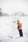 Niña paleando nieve frente a muñeco de nieve, Lakefield, Ontario, Canadá - foto de stock