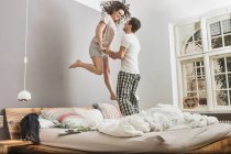 Couple en pyjama sautant sur le lit — Photo de stock