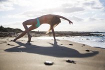 Junge Frau am Strand, in Yogaposition, Rückansicht — Stockfoto