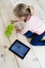 Девушка с цифровым планшетом, играющая в игрушки на деревянном полу — стоковое фото