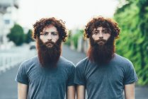Portrait de jumeaux mâles adultes identiques aux cheveux roux et barbe sur le trottoir — Photo de stock