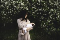 Взрослая женщина, несущая дочку на руках у садового яблока — стоковое фото