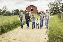 Vista frontale a tutta lunghezza della famiglia multi generazione che cammina su pista sterrata in fattoria — Foto stock