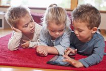 Два мальчика и девочка с помощью цифрового планшета в детской школе — стоковое фото