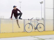 Urban cyclist climbing over fence on sports field — Stock Photo
