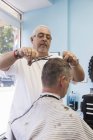 Barber cutting male client hair in salon — Stock Photo