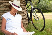 Seniorin lehnt im Park an Palme beim Lesen — Stockfoto