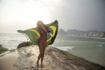 Young woman holding up Brazilian flag,  Ipanema beach, Rio De Janeiro, Brazil — Stock Photo