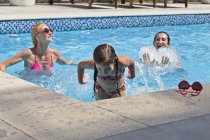 Joven familia jugando en la piscina al aire libre - foto de stock