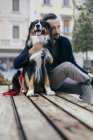 Mid adult man sitting with pet dog on city square bench — Stock Photo