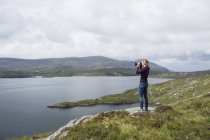 Donna che fotografa vista, in piedi sulla riva nord di East Loch Tarbet, North Harris, Ebridi Esterne, Scozia — Foto stock