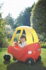 Female toddler playing in toy car in the garden — Stock Photo