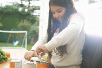 Девушка за кухонным столом открывает банку томатного супа — стоковое фото